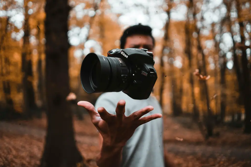 Photographer tossing a DSLR camera in an autumn forest for brand photography and visual storytelling